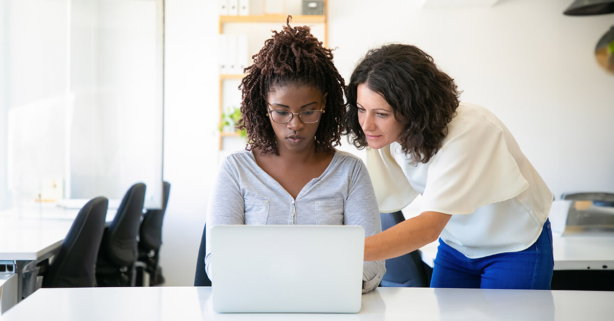 Woman assisting a younger woman completing online forms on a laptop