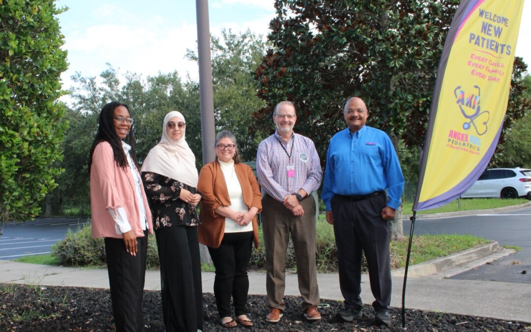 Five Angel Kids Pediatrics team members standing outside next to a Welcome New Patients banner