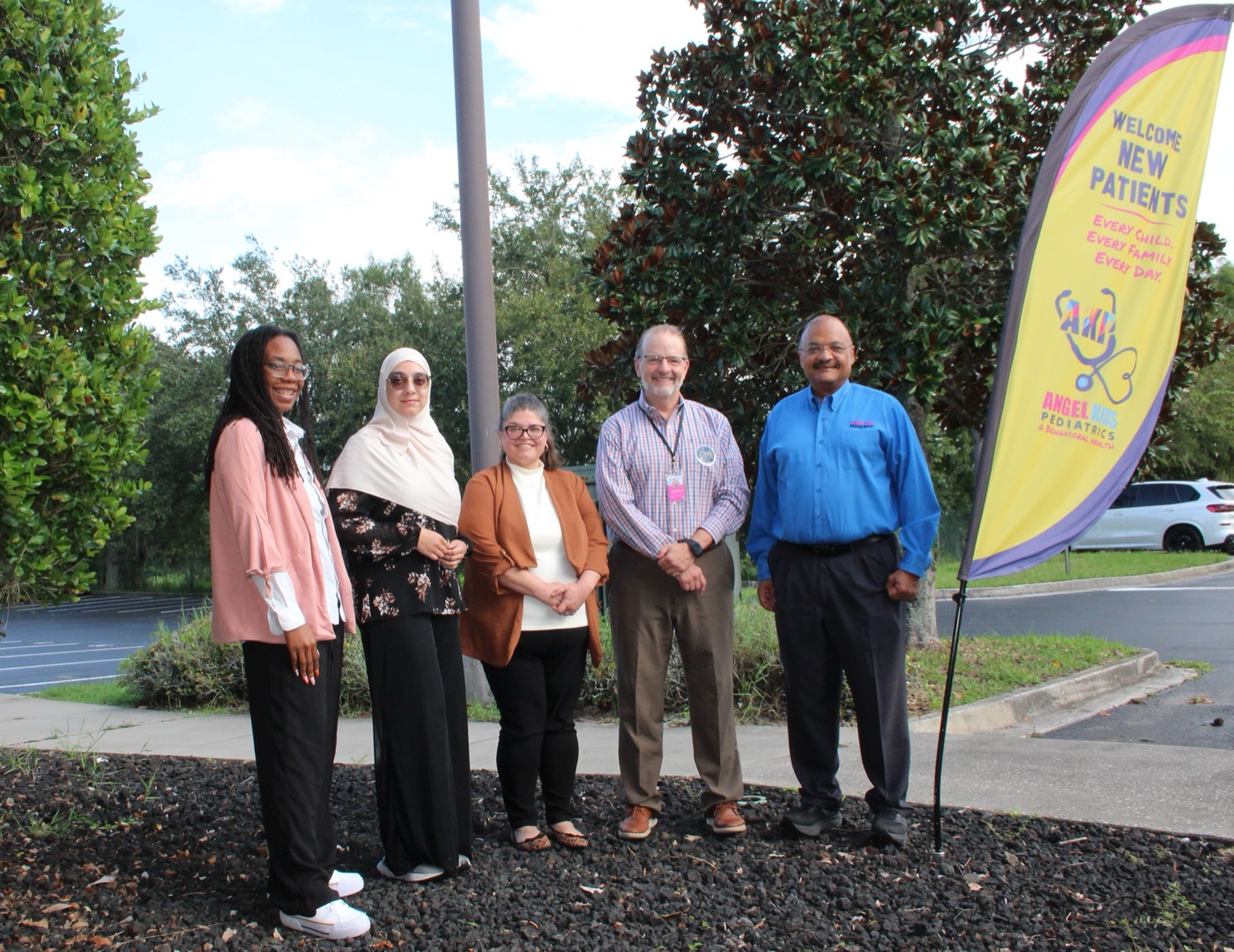 Five Angel Kids Pediatrics team members standing outside next to a Welcome New Patients banner