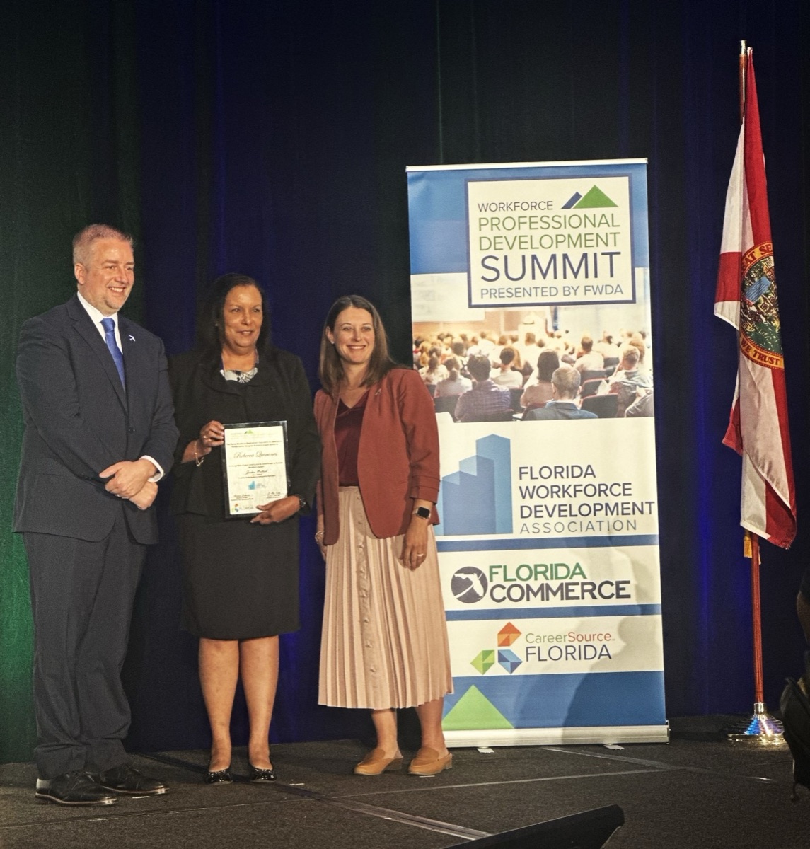 Joshua Matlock, Rebecca Quinones holding her nomination certificate, and Adrienne Johnston on stage at the FWDA Workforce Summit