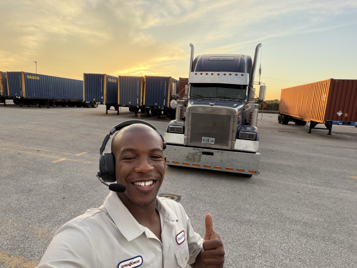 Joshua Theagene smiling in front of a semi truck at a container yard